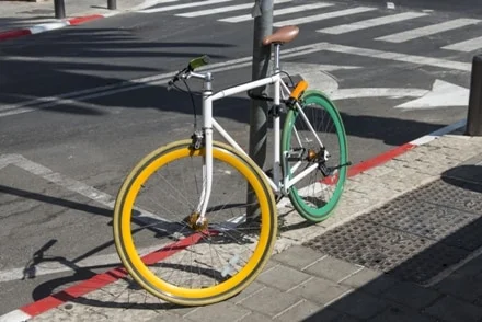 a colored bicycle locked to a post on the pavement 1