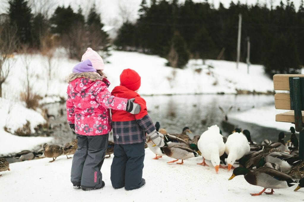 child in red and blue plaid jacket and black pants standing on snow covered ground during